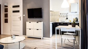 A modern kitchen with a flat-screen TV, white cabinets, and a dining area with a table and chairs. - Pory Mokotow Apartment (Warsaw)