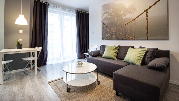 A modern living room with a sofa, a coffee table, a dining table, and a painting of a bridge. - Pory Mokotow Apartment (Warsaw)