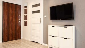 A room with a wooden door, a white cabinet with drawers, and a mounted flat-screen TV on the wall. - Pory Mokotow Apartment (Warsaw)