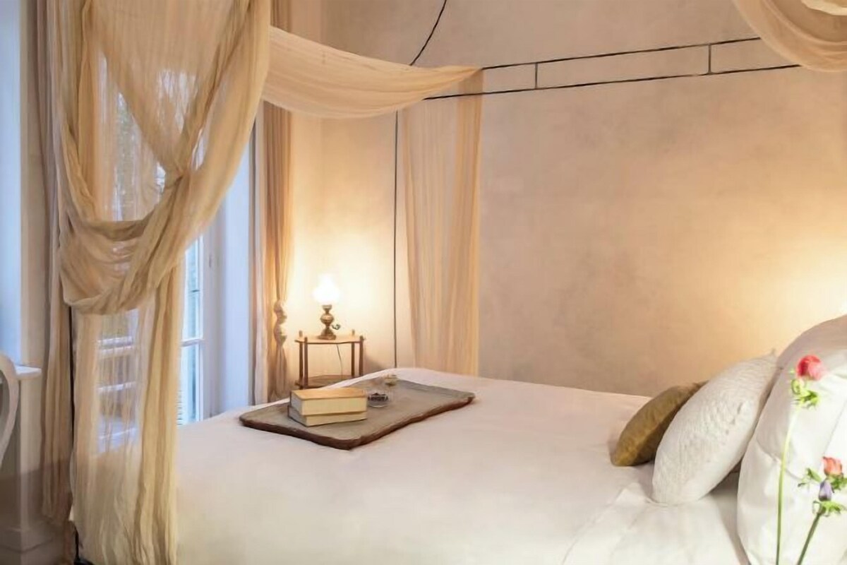 A bedroom with a bed, a bedside table with a lamp, a book, and a decorative pillow.