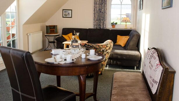 Een eetgedeelte met een ronde tafel voor vier personen, een bank en een raam met gordijnen.
