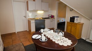 Een kleine keuken met witte kasten, een eettafel gedekt met borden, bekers en een waterkoker, en een magnetron op een houten kast.
