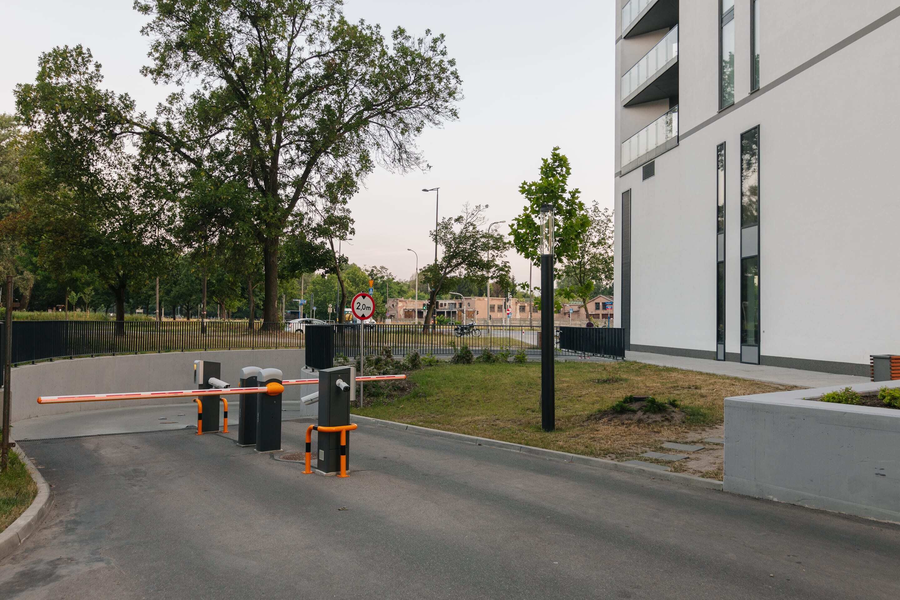 Un bâtiment moderne doté d’une entrée sécurisée par un portail, d’un passage piéton et d’un panneau indiquant une hauteur maximale de 2,0 mètres.