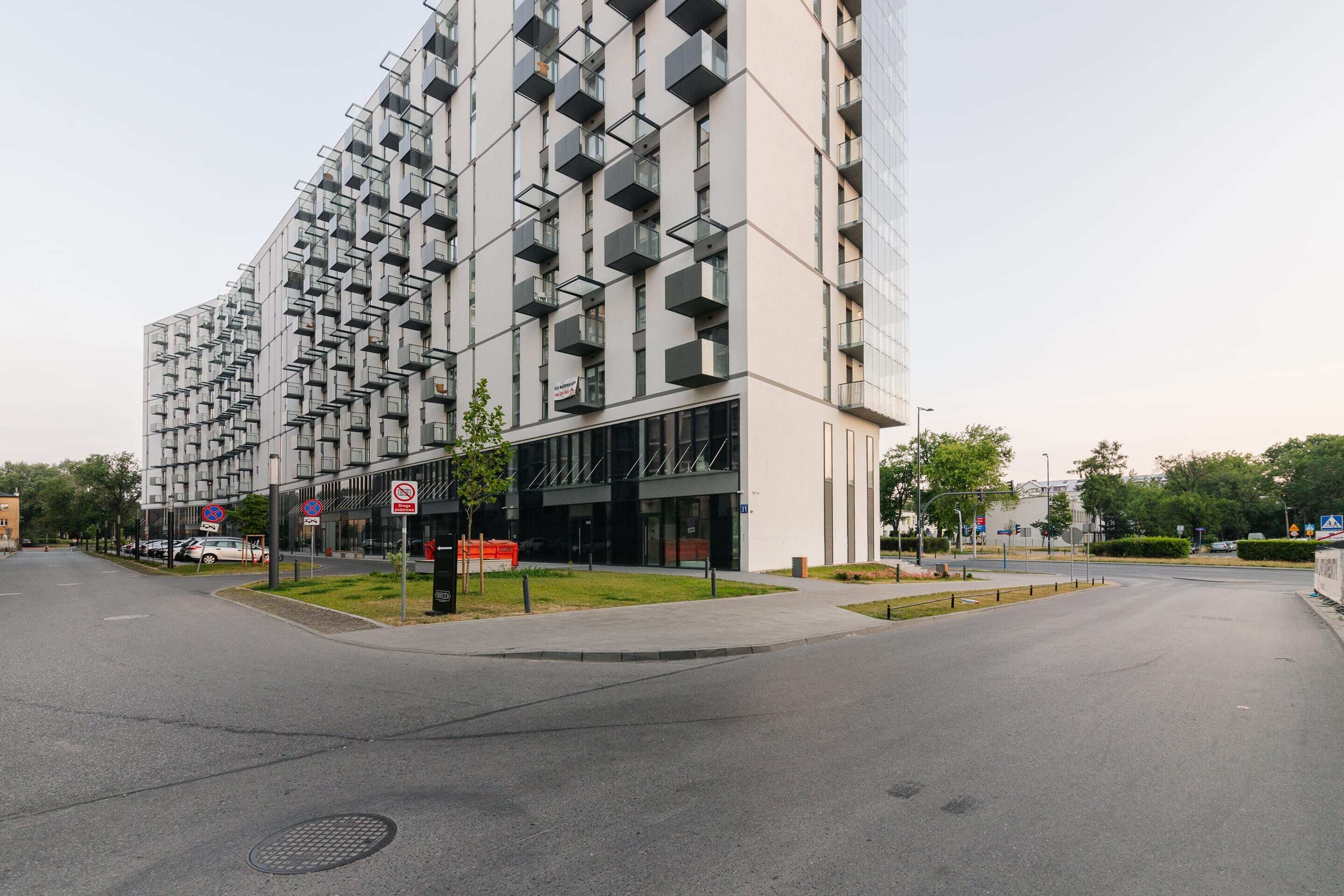 Een modern gebouw met een unieke geometrische gevel, een voetpad en een verbodsbord voor geparkeerde voertuigen.