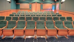 A theater with rows of green cushioned seats and a dark floor. - Fiji Palms (Kissimmee)