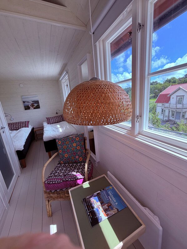 A room with a bed, a chair, a table, and a window with a view of a house. - Hem Till Bengt (Kungshamn)