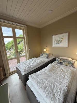 A room with two beds, a window with a view of greenery, a wall-mounted lamp, and a framed picture. - Hem Till Bengt (Kungshamn)