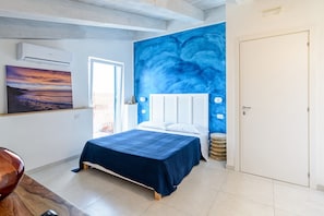 A bedroom with a bed, a large blue mural, an air conditioning unit, and a door. - Il Colore del Mare (Agropoli)