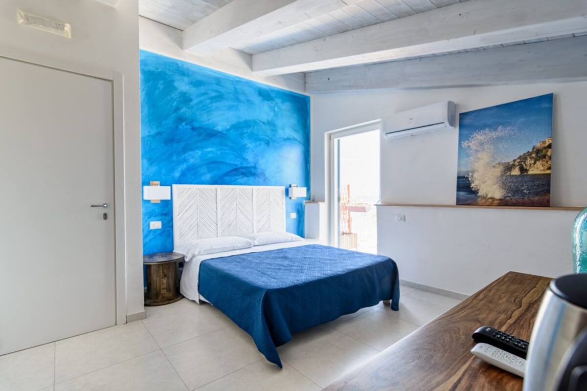 Un dormitorio con una cama, una mesa de madera, un cuadro de una escena costera y una puerta blanca.