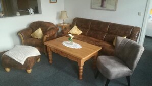 Een woonkamer met een bruine leren bank, een houten salontafel en een grijze fauteuil.