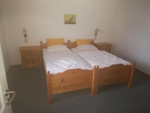 Une chambre avec un lit simple, un cadre de lit en bois, deux tables de chevet et une petite lampe de chevet.