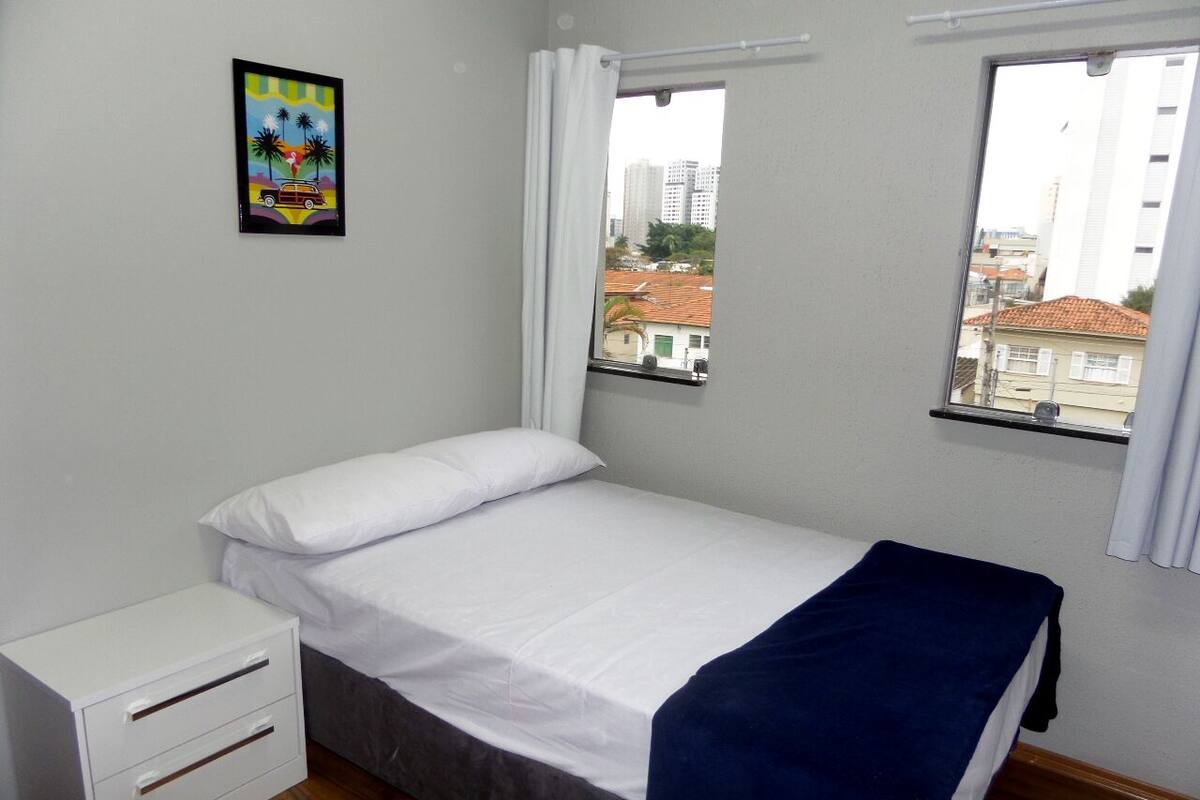 Ein Schlafzimmer mit Bett, Nachttisch und Fenster mit Blick auf Gebäude.