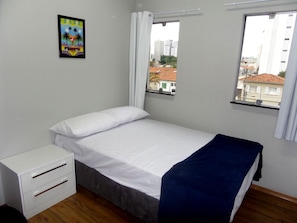 A bedroom with a bed, a nightstand, and a window with a view of buildings. - Visto Hostel (São Paulo)