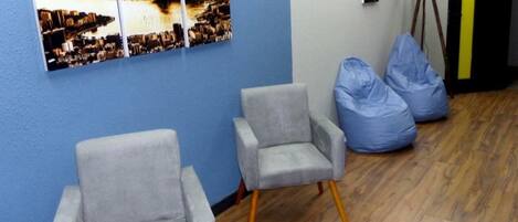 Una habitación con dos sillones grises, un sillón inflable azul, un televisor y una pared con un cuadro de un paisaje urbano al atardecer.
