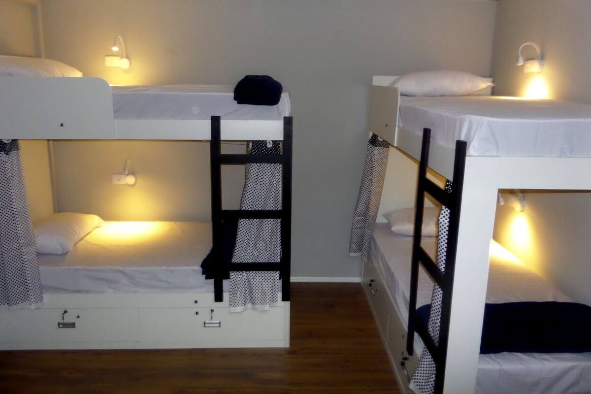 Etagenbetten mit daran angebrachten Schreibtischen und Stauraumfächern, jeweils mit einer kleinen Lampe.
