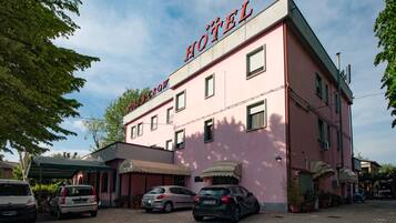 Un edificio rosa con un letrero que dice "Rose & Crow Hotel". Hay varios coches estacionados frente al edificio, el cual tiene múltiples ventanas y una entrada cubierta.