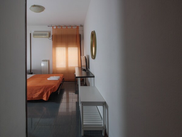 Habitación de hotel con cama, escritorio, silla, aire acondicionado y ventana con persianas.