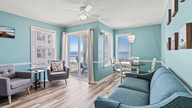 A living room with a grey sofa, a blue sofa, a small table, and a ceiling fan. - Recently Renovated Oceanfront Condo in Windy Hill + Free Attraction Tickets! (North Myrtle Beach)