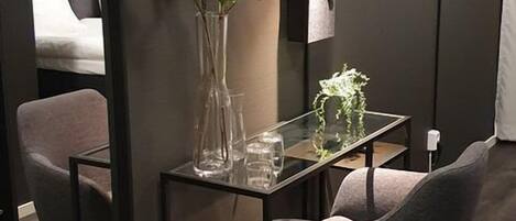 A modern room with a dark wall, a glass table, a chair, a mirror, and a plant.