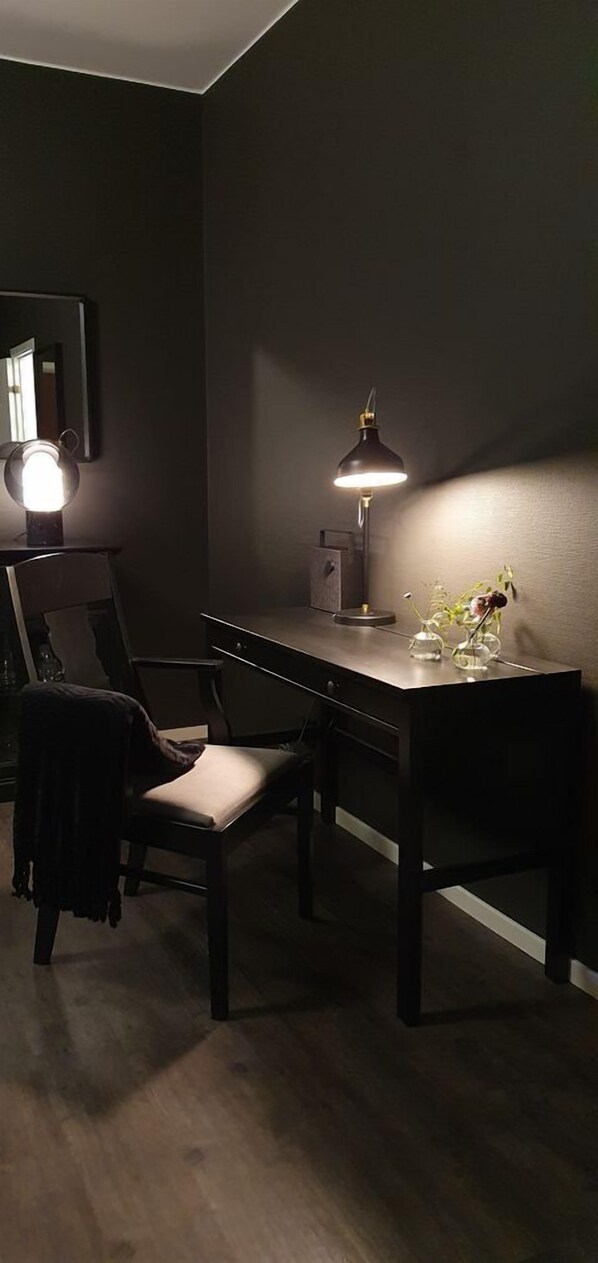 Una habitación de tonos oscuros con un escritorio, una silla y una lámpara de escritorio.