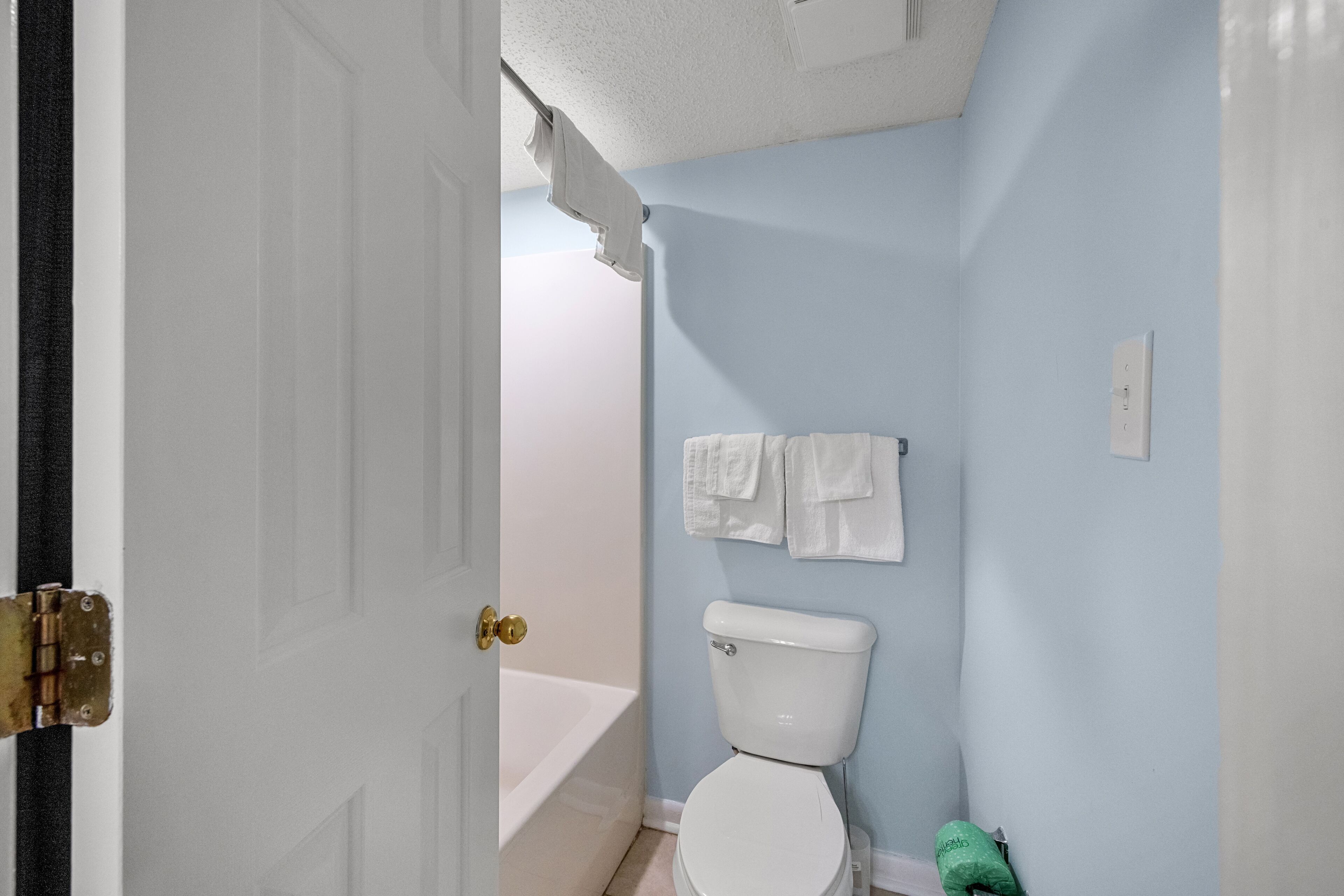 Un baño con un inodoro blanco, una bañera y un perchero con dos toallas.
