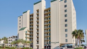 A multi-story hotel with balconies, a sign reading "Beach Club", and a parking area with cars. - Spacious 1st floor corner Oceanfront unit + Free Attraction Tickets! (North Myrtle Beach)