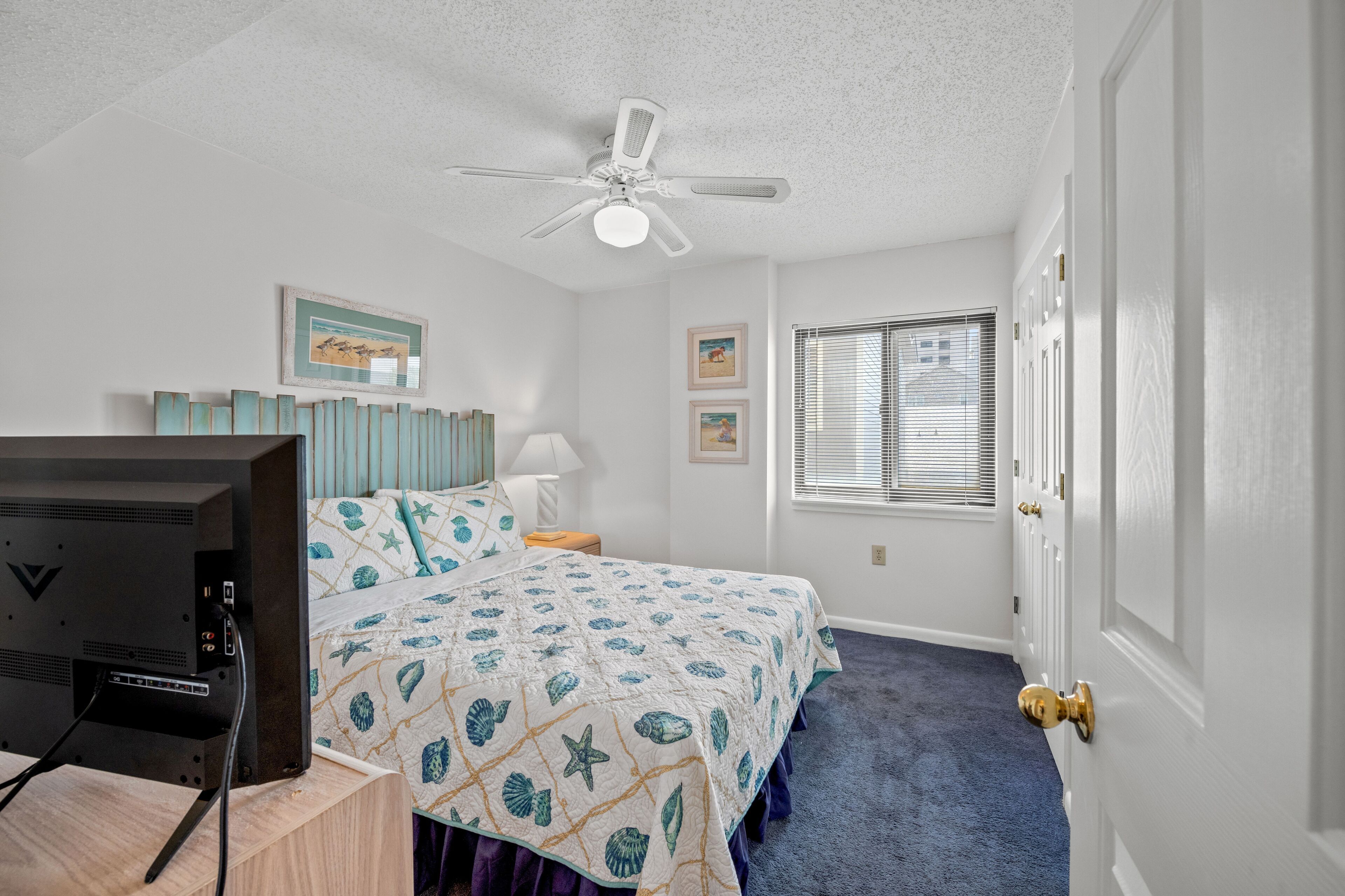 A bedroom with a bed, a ceiling fan, a TV, and a window with blinds.