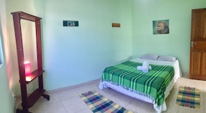 A bedroom with a bed, a nightstand, a mirror, a green and white checkered blanket, and a welcome sign. - Casa Centro Histórico (Paraty)