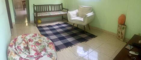 A room with a checkered rug, a floral bean bag, a wooden bench, a white armchair, and a small table with electronic devices.