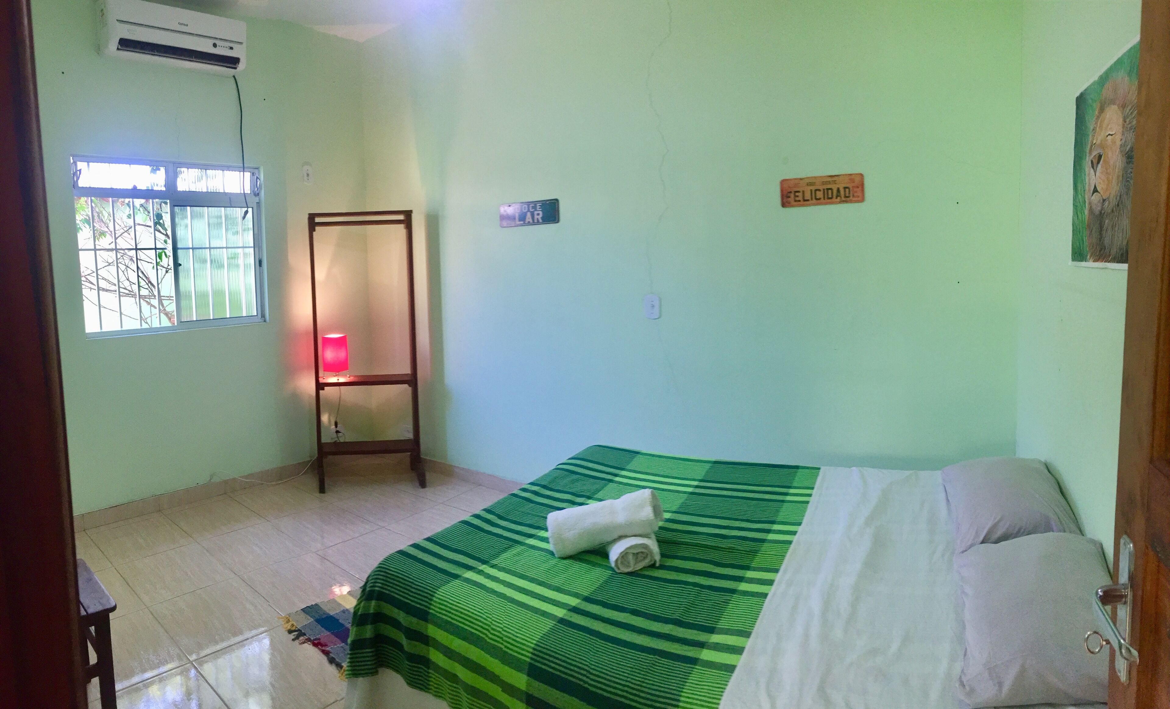 A room with a bed, a standing lamp, a welcome sign, and a window with bars.