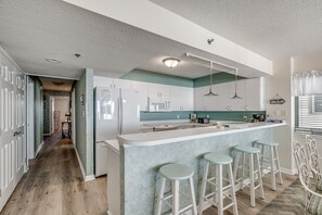 Uma cozinha moderna com uma ilha central, banquetas e vista para a área de jantar adjacente.