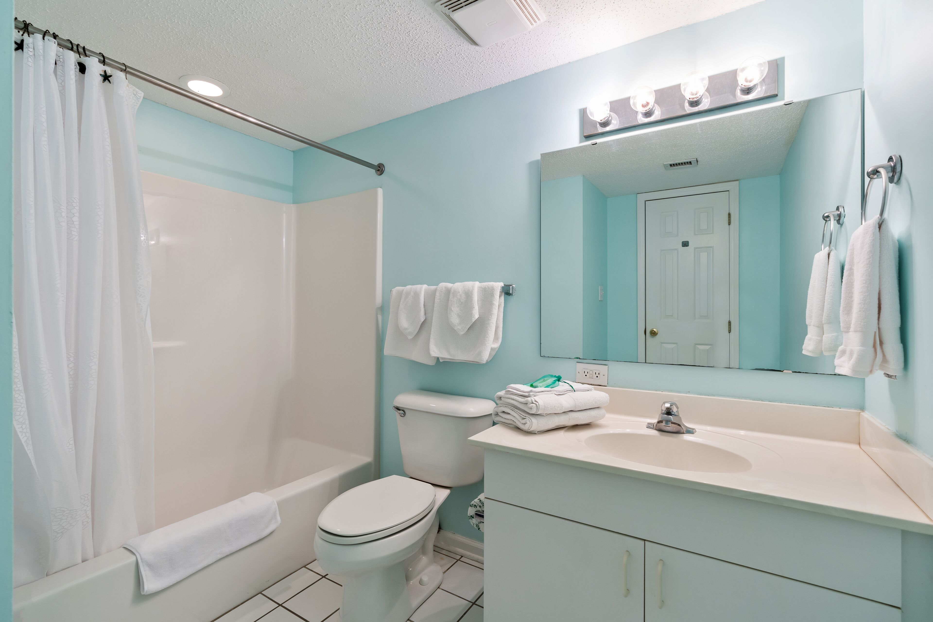 A bathroom with a shower, toilet, sink, and a mirror with lights.