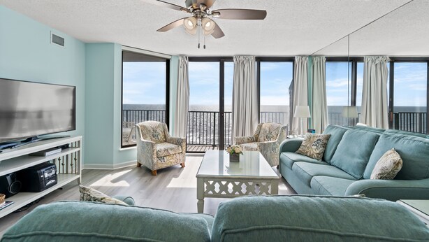 A living room with a TV, sofa, chairs, and a ceiling fan. - Recently updated oceanfront unit, wonderful views + Free Attraction Tickets! (North Myrtle Beach)