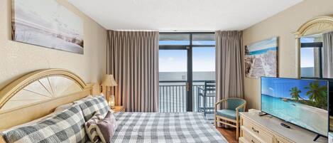 A hotel room with a bed, a television, a chair, and a balcony with a view of the sea.