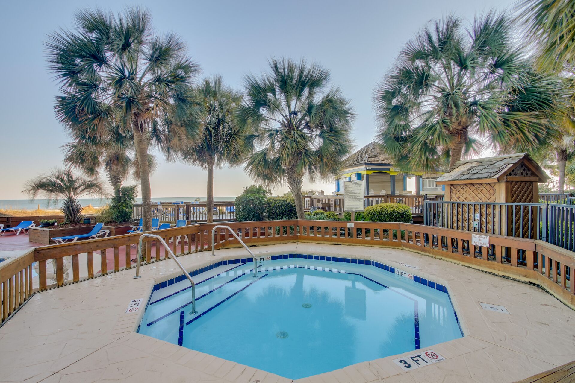 A swimming pool with a wooden deck, palm trees, and lounge chairs.