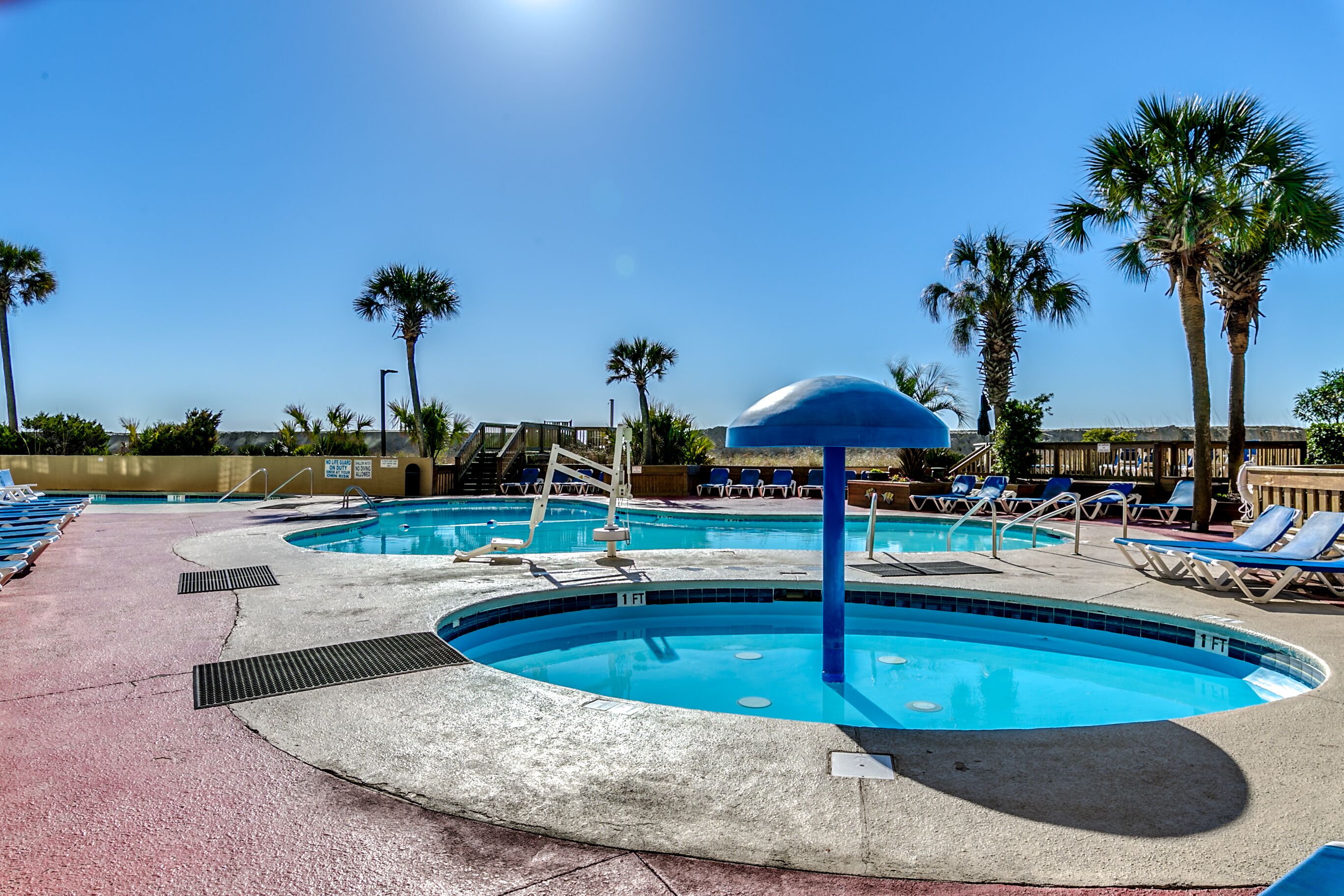 Un área de piscina con varias piscinas, sillas de descanso y palmeras.