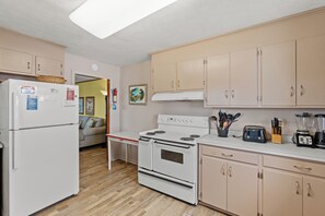 A kitchen with a refrigerator, stove, and various appliances. There is a dining table and a sofa in the background. - Pet Friendly Oceanfront Duplex (bottom floor) + Free Attraction Tickets! (North Myrtle Beach)