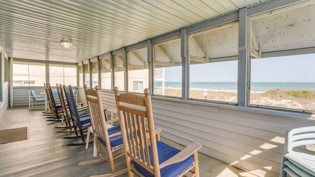 Une véranda couverte avec des fauteuils à bascule en bois et une vue sur la plage.