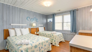 Une chambre avec deux lits, des murs en bois, une fenêtre avec des rideaux et une petite table.