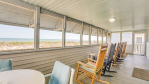 Un espace extérieur abrité, aménagé avec des chaises en bois et une table, et offrant une vue sur la plage.