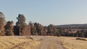 Paisaje rural con un pequeño edificio de ladrillo, posiblemente una casa o construcción, rodeado de árboles y campos abiertos.
