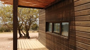 Fachada de madera con un pérgola, una ventana y un árbol de fondo.
