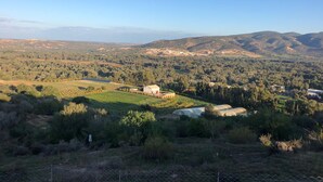 Paisaje rural con campos, una casa de campo y colinas a lo lejos.