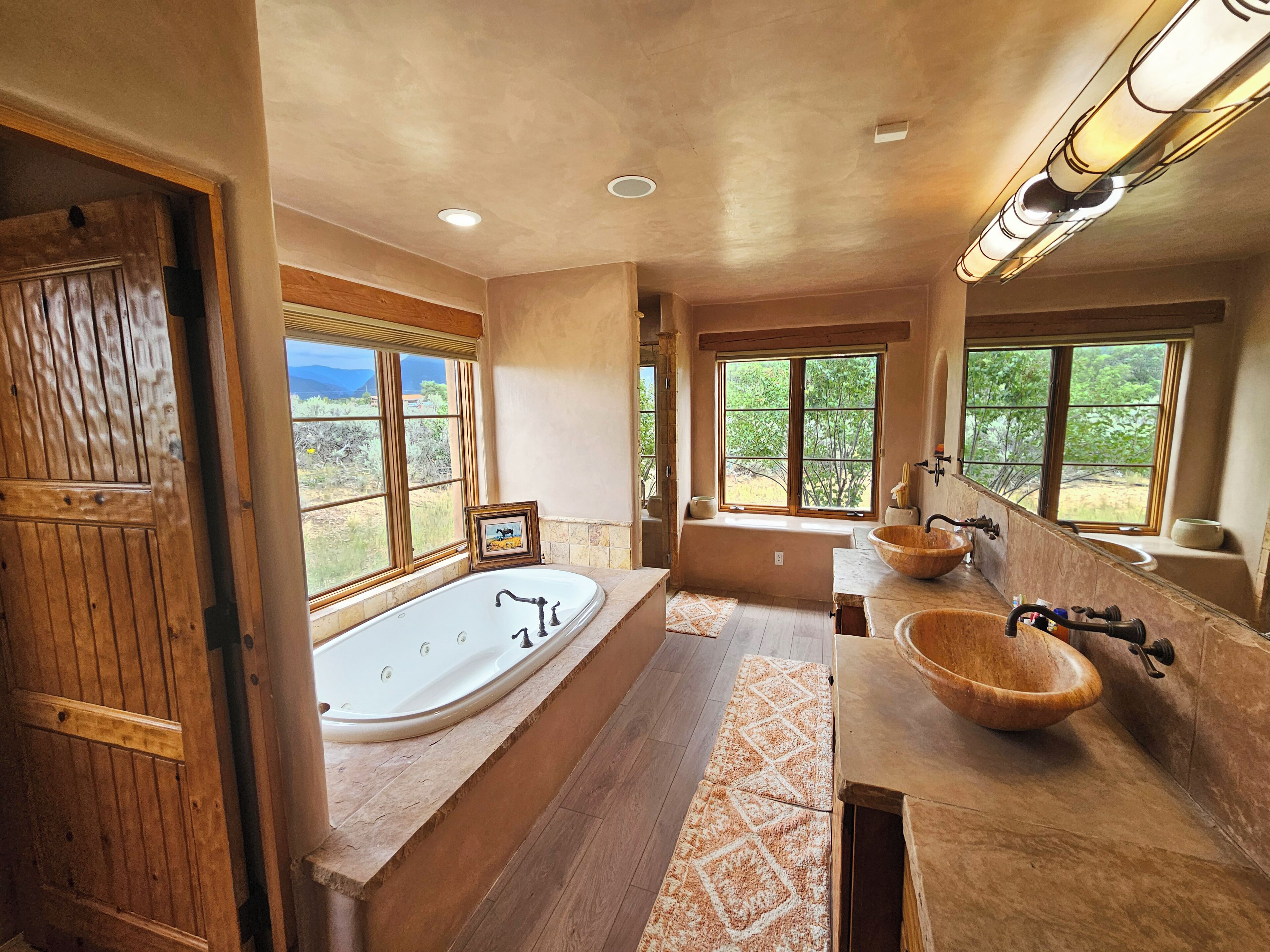 Un baño espacioso con una bañera grande, dos lavamanos de madera y ventanas amplias que ofrecen vistas al exterior.
