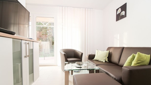A modern living room with a glass coffee table, a brown leather sofa, and a dining area with a chair. - Well-kept apartment in Greetsiel (Greetsiel)