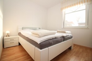 A neatly made bed with pillows and a blanket, a bedside table with a lamp, and a window with curtains.