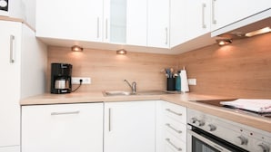A modern kitchen with white cabinets, a built-in oven, and a coffee maker. - Well-kept apartment in Greetsiel (Greetsiel)