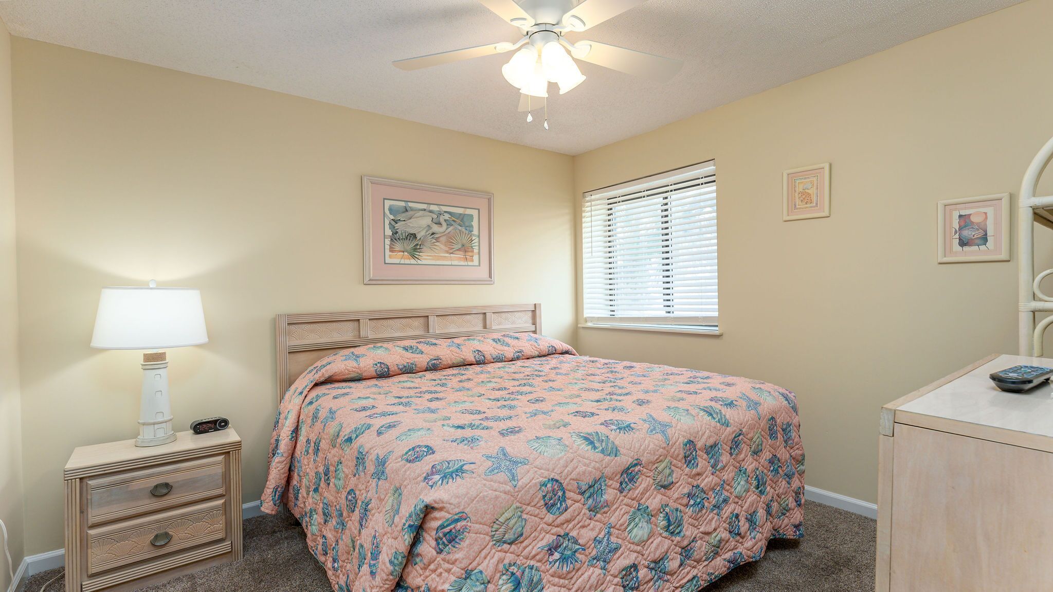 A bedroom with a bed, a nightstand, a lamp, a window with blinds, and a ceiling fan.