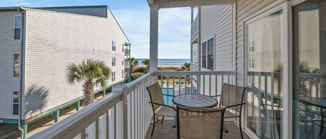 A balcony with a table and chairs, overlooking a beach and other buildings.