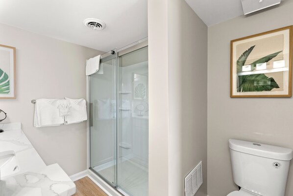 Une salle de bain moderne dotée d’une douche à parois de verre, de toilettes et d’un lavabo avec un plan de travail en marbre.